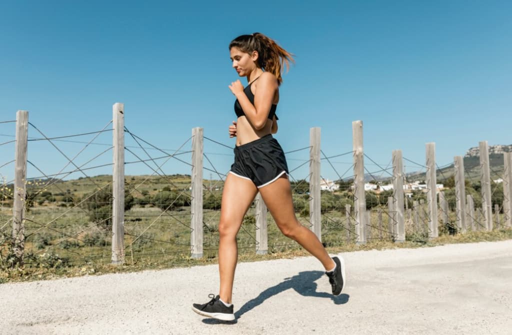 A woman running on a dirt road beside a fence in sunny weather