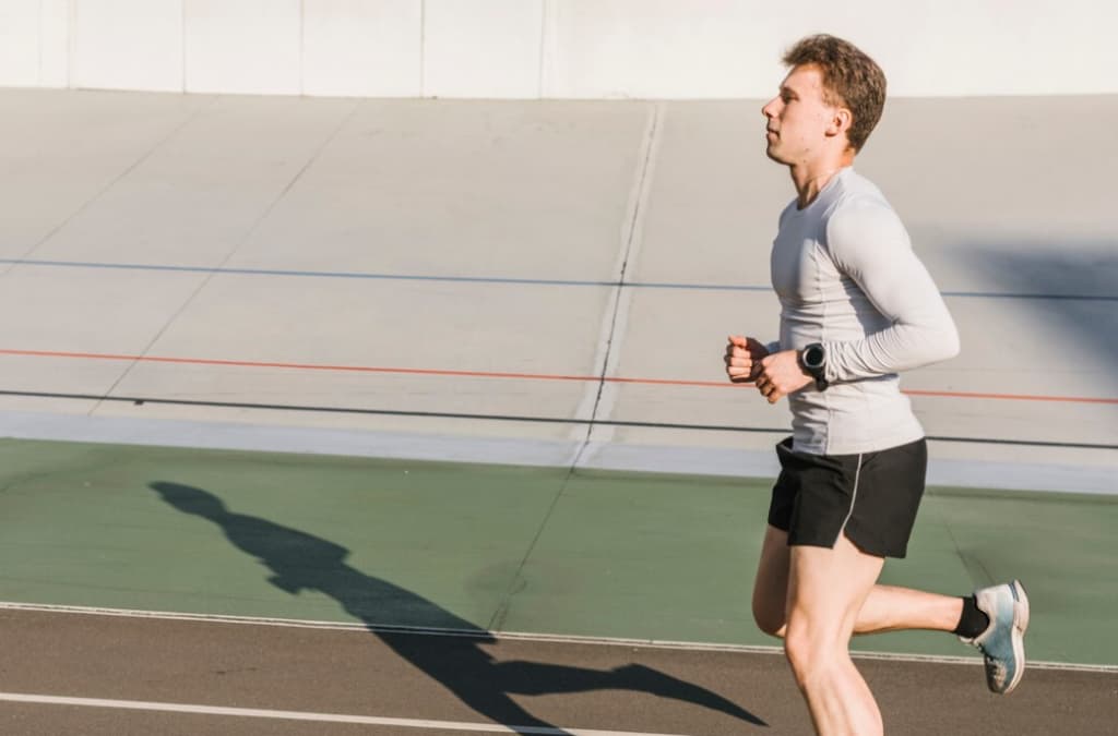 An athlete running solo on an outdoor track, casting a long shadow