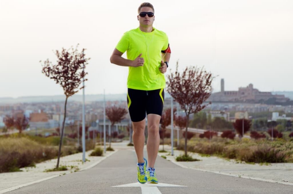 A man jogging on a pathway in bright neon clothing and sunglasses