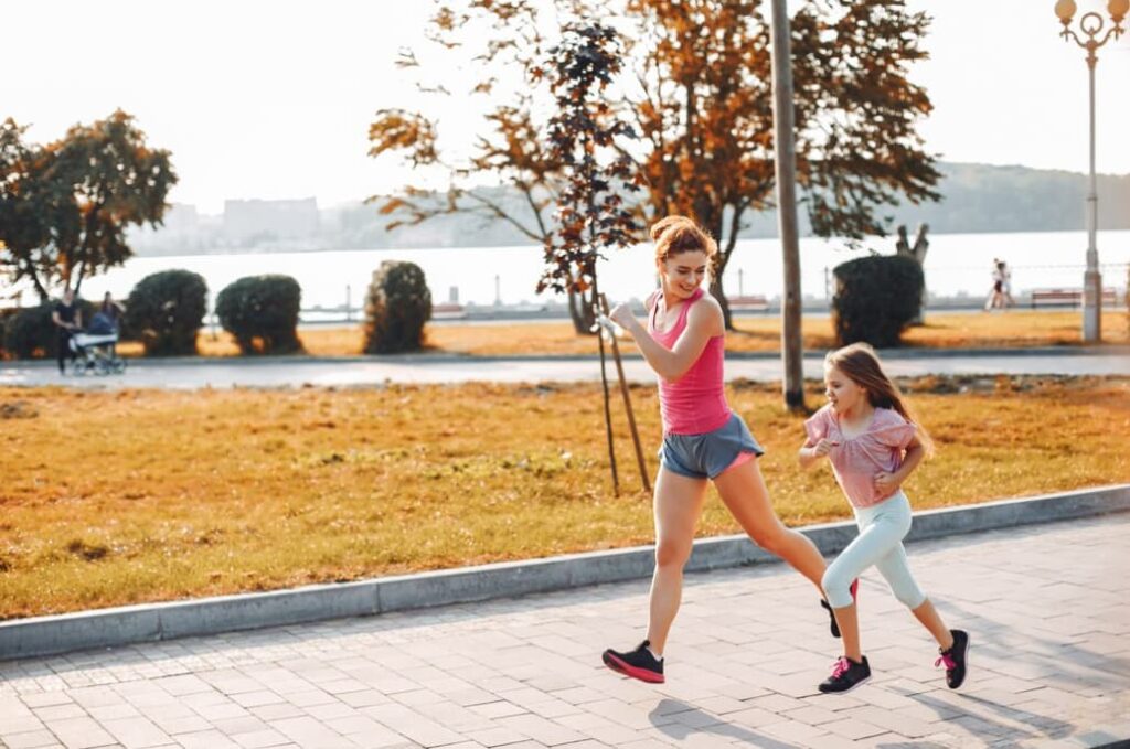 A woman in sportswear jogs with a girl by the lakeside, basking in the sun's glow