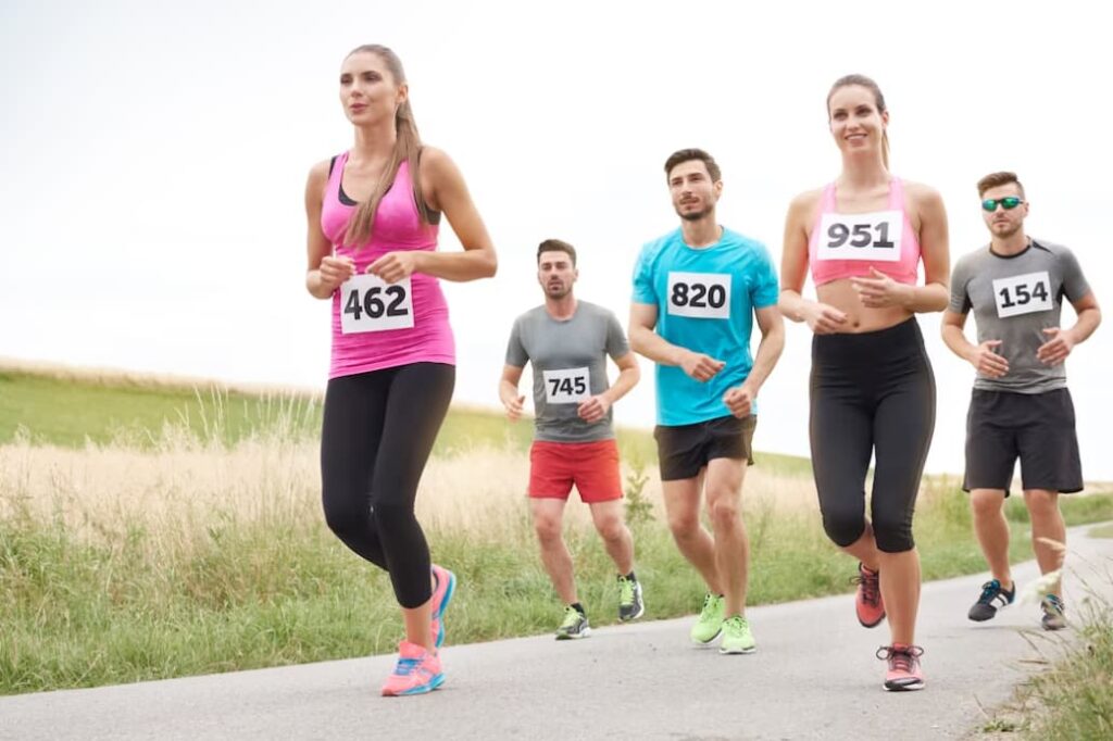 five runners with bibs compete on a road, the grass on the sides