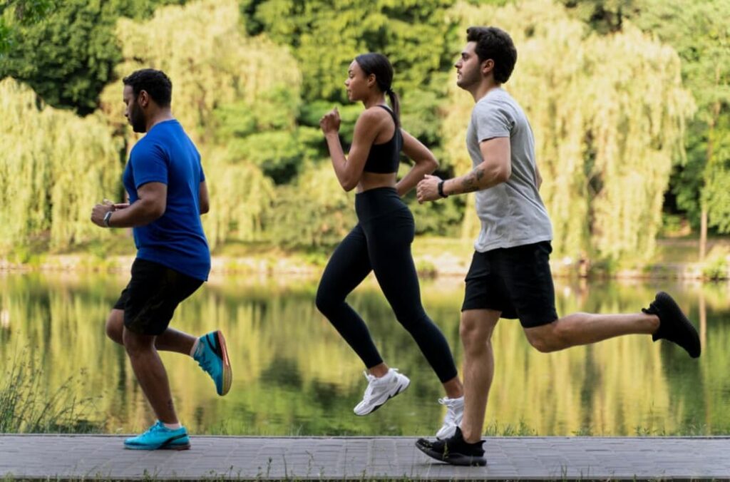 A group of three jog by a calm lakeside with lush greenery